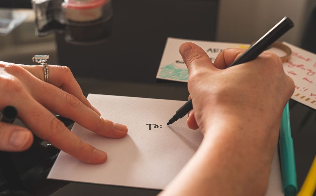 Hands writing a gift note on an envelope.